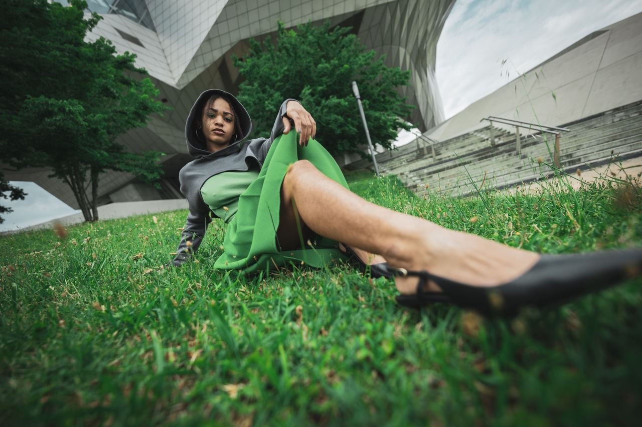 Stylish woman in green dress posing outdoors near modern architecture, conveying a fashion-forward aesthetic.